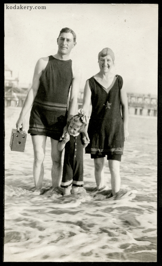 Vintage snapshot of a 1920s family in the surf, with the man holding a period box camera
